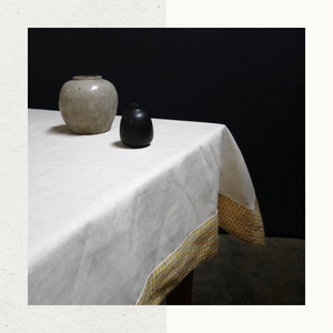 A table set with vases and linens, featuring a Cloth Edition tablecloth in natural high quality Belgian linen with a block print border in yellow